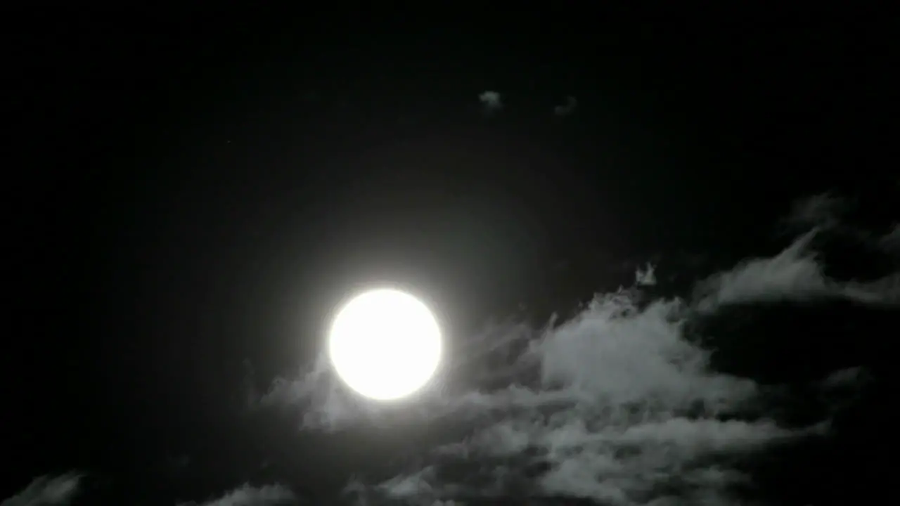 A bright full moon rises above swiftly moving clouds in the night sky