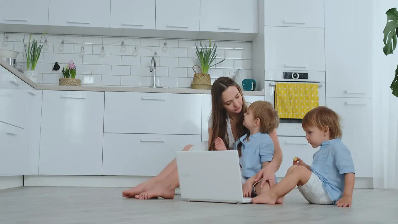 Una Madre Amante De Un Apartamento Moderno Y Dos Hijos Pequeños Sentados En El Suelo De La Sala De Estar Miran La Pantalla Del Portátil Los Niños Con Mamá Juegan En Una Computadora Portátil