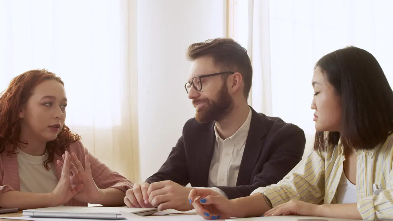 Grupo De Tres Colegas Multiétnicos Sentados A La Mesa Y Debatiendo Sobre El Trabajo 2