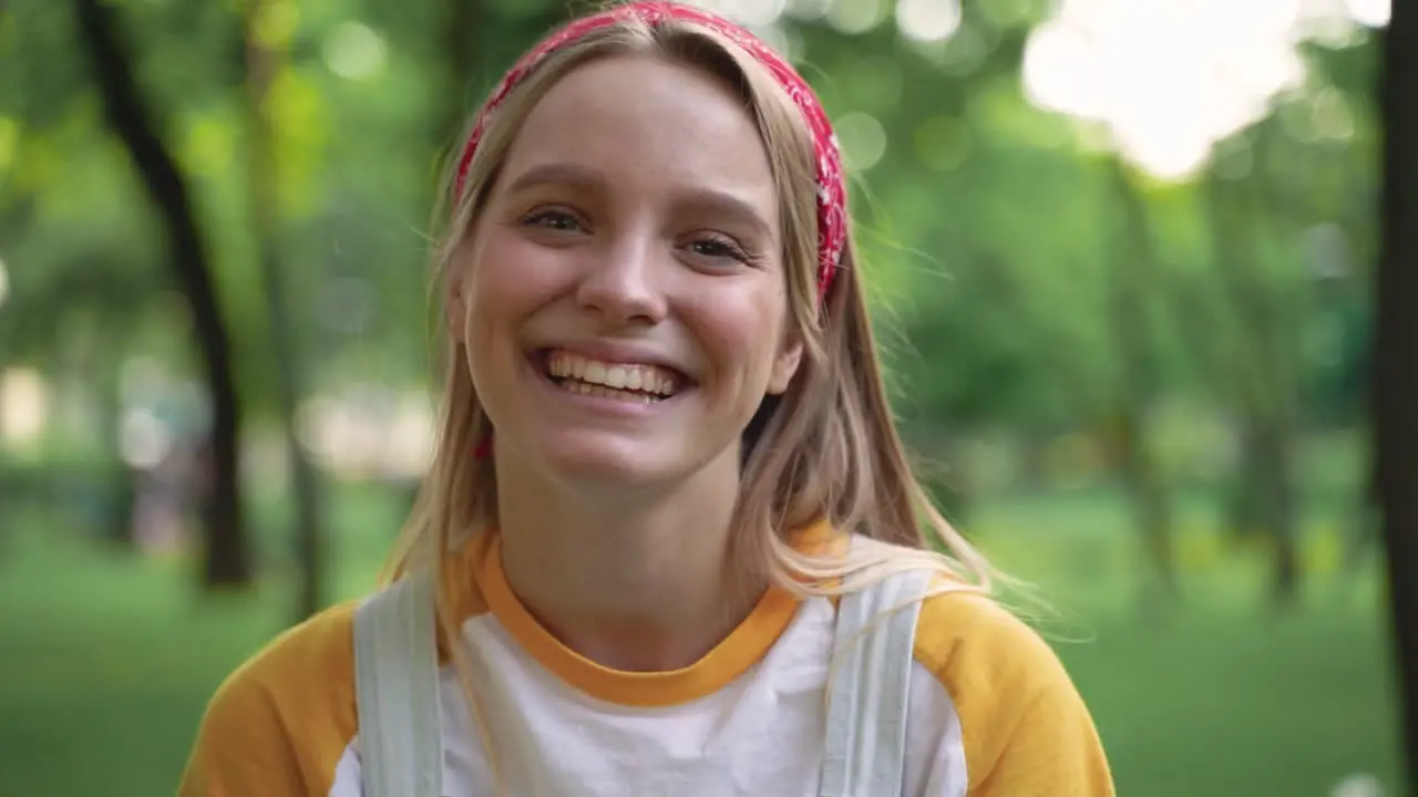 Retrato De Una Chica Muy Alegre Sonriendo A La Cámara Señalando Su Sonrisa Y Guiñando Un Ojo Al Aire Libre