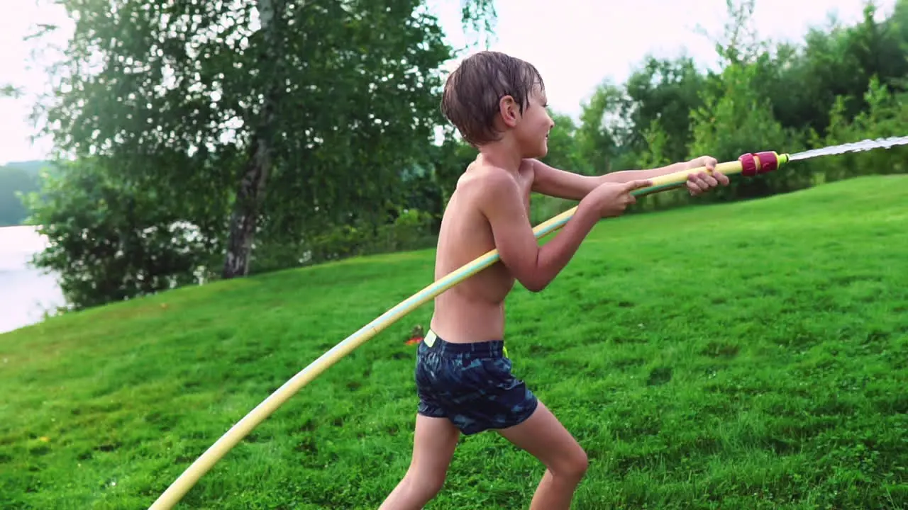 Un Niño En Bañador De Verano Vierte Agua Sobre Su Hermano Menor Divirtiéndose En El Parque En El Césped Cerca Del Lago