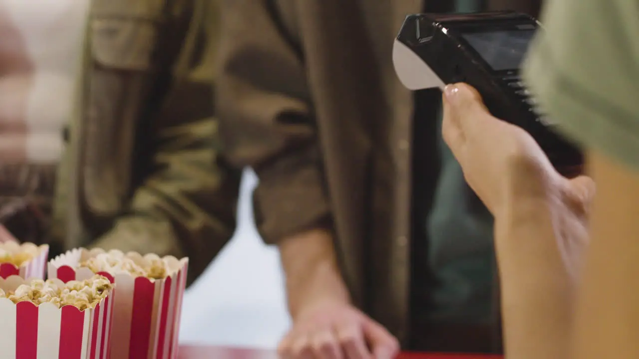 Close Up Of An Unrecognizable Woman Paying With Phone At The Ticket Counter In The Cinema Hall