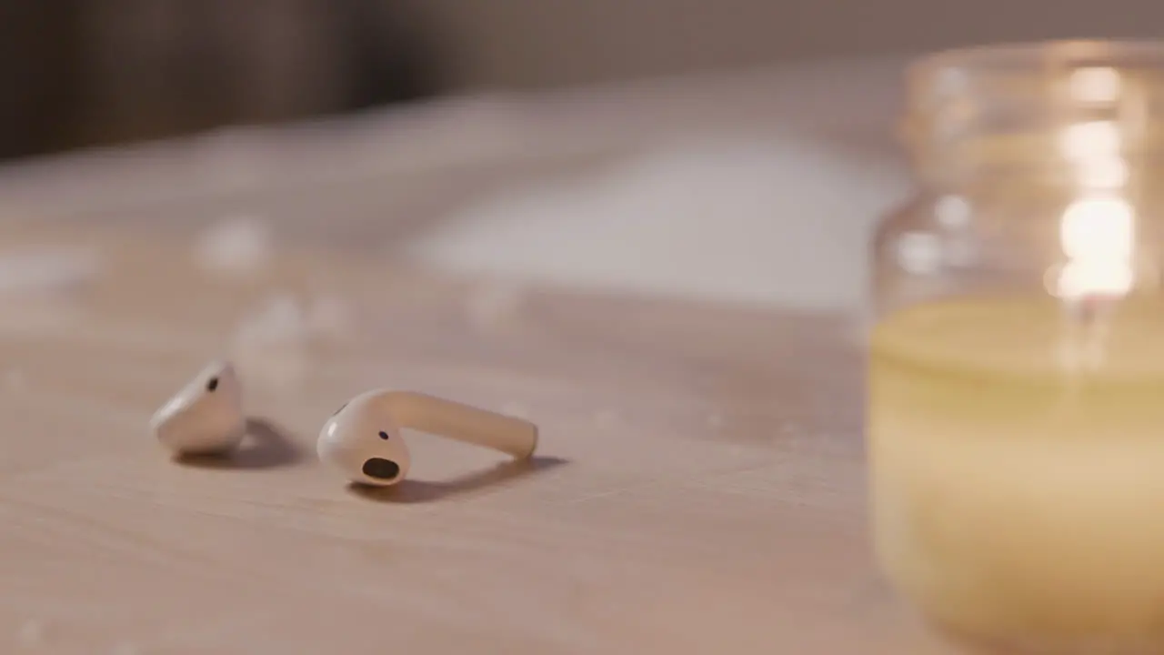 Close Up View Of Earphones And A Candle On Top Of A Wooden Table In The Background A Blurred Bathtub Filled With Water And Foam