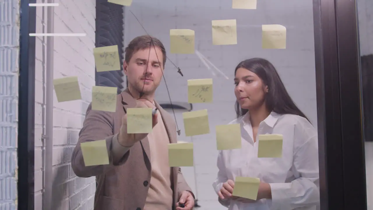 Businessman And Businesswoman Brainstorming With Sticky Notes On Glass Window 2