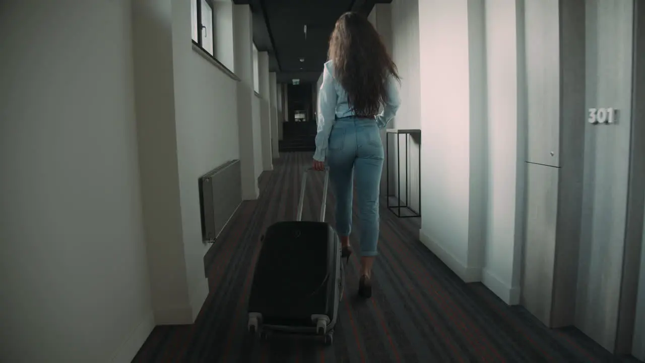 Young woman rolling suitcase in hotel corridor Slim girl crossing hotel space