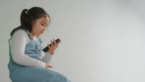 Studio Shot Of Young Girl On ASD Spectrum Gaming On Mobile Phone Against White Background