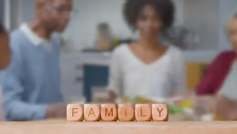 Concept With Wooden Letter Cubes Or Dice Spelling Family Against Background Of People Eating Meal At Home