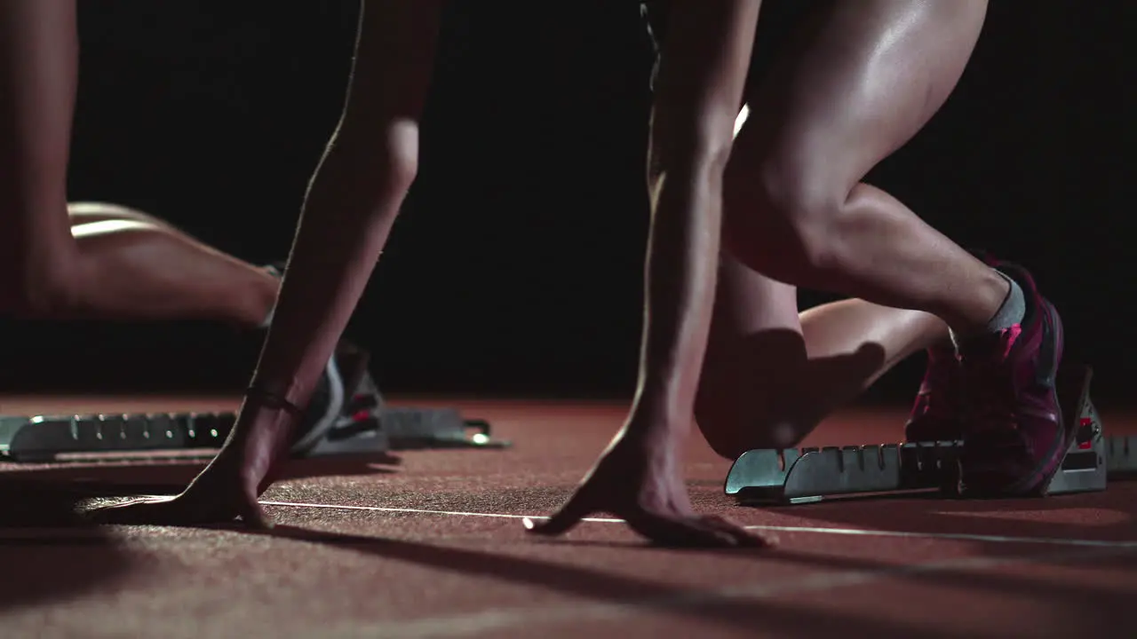 Female runners at athletics track crouching at the starting blocks before a race In slow motion