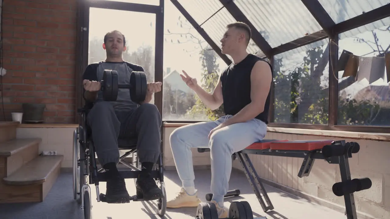 Disabled Man In Wheelchair Working Out With Dumbbell At Home While His Personal Trainer Motivating Him