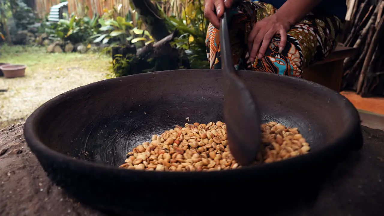 Medium slow motion shot of roasted coffee beans kopi luwak while the beans are stirred and roasted in a wok with a wooden spoon by one of the coffee plantation's employees in Bali indonesia