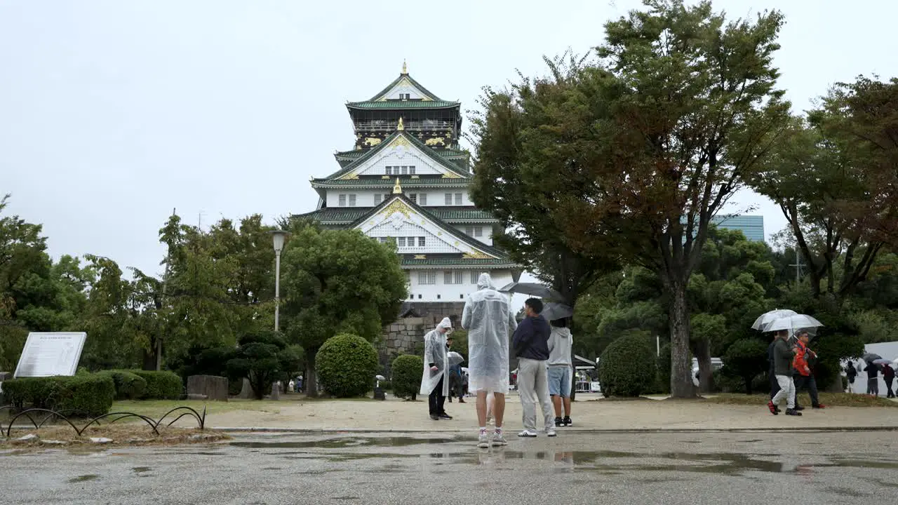 Tourists Wearing Rain Poncho's Taking Photos Of Osaka Castle On Rainy Overcast Day In Osaka