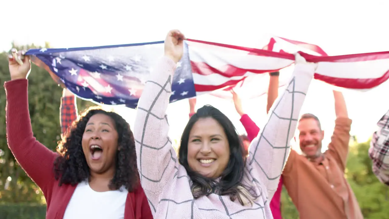 Happy diverse male and female friends dancing with flags in sunny garden