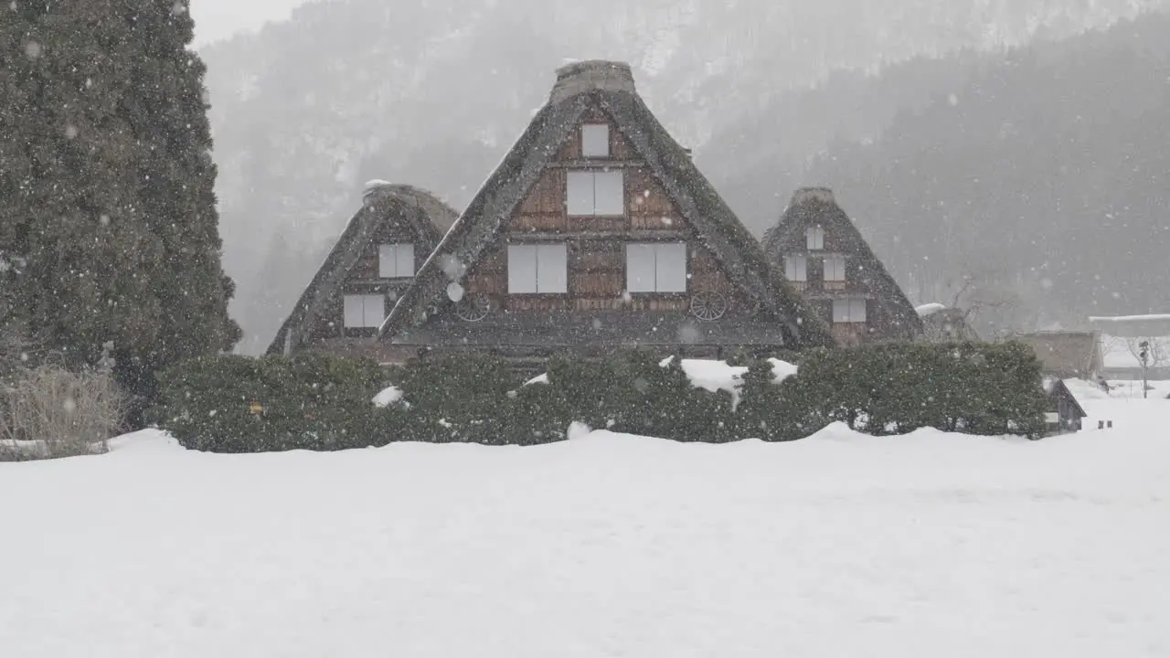 A slow motion shot of three houses under the snow in the small village of Shirakawago during winter in Japan