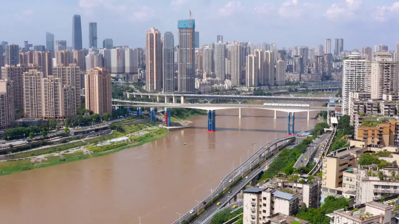 Dolly push in tilt up reveals Chongqing city china skyline and murky brown river blue sky day aerial