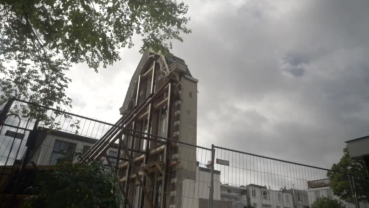 The facade of a classic Amsterdam building With Trees Swaying in the Foreground and Cloudy Skies