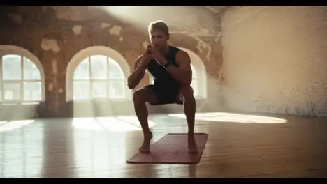 A man in a black sports uniform does exercises and squats developing calf muscles on a special carpet in a sunny hall