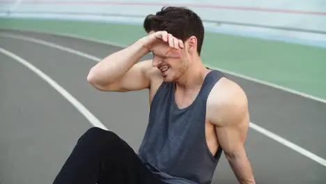 Close up of exhausted man sitting on stadium track Sport man resting