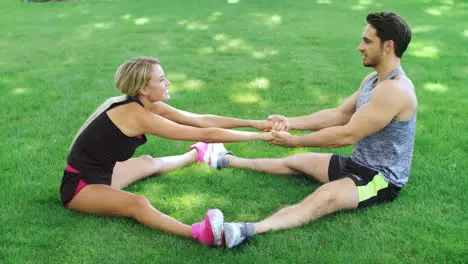 Happy couple man and woman doing stretching exercise on grass in summer park