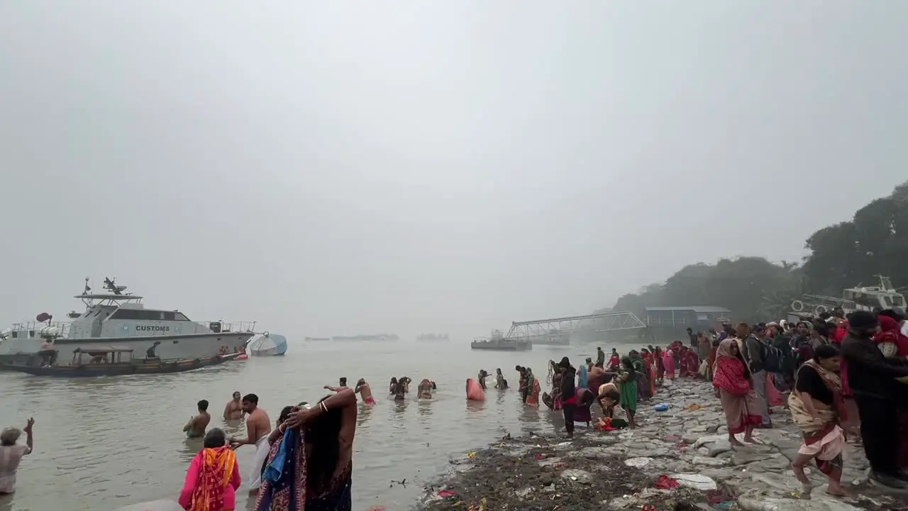 Wide shot of men and woman bathing and praying in foggy winter morning during Sankranti with jetty in the background