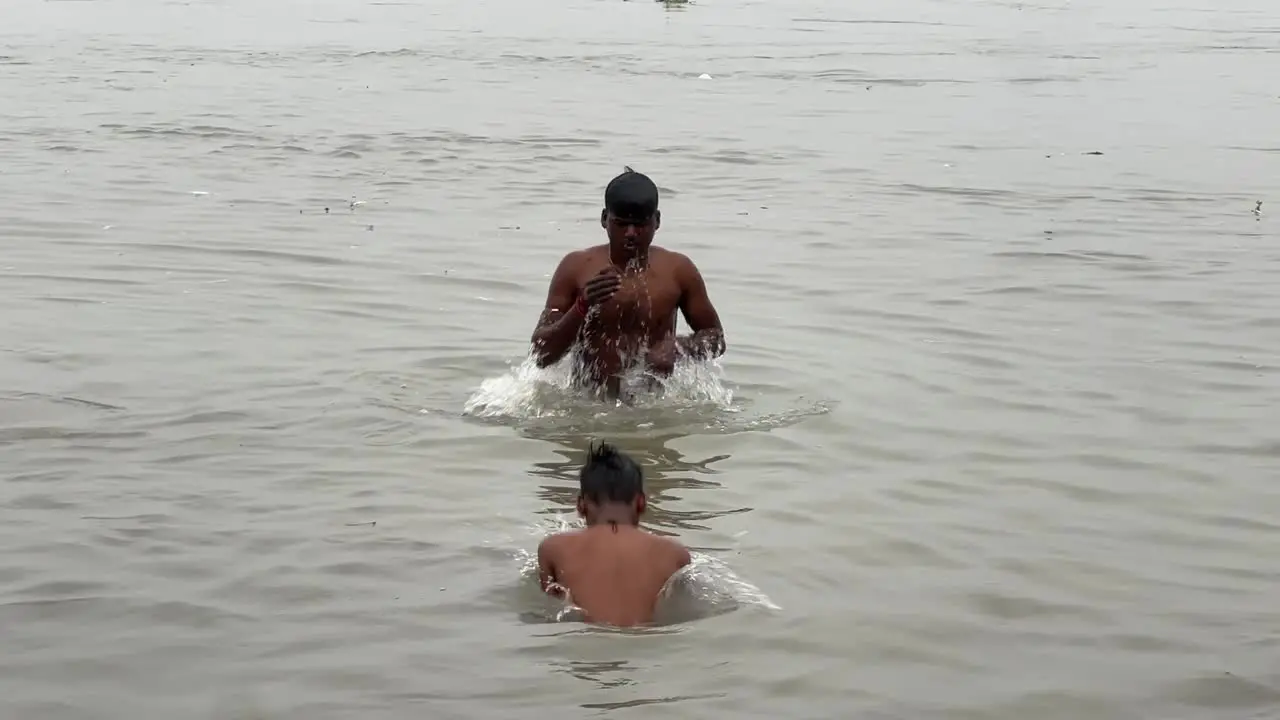 Two boys bathing and taking holy ganga water in bottle during Sankranti Hindu festival in Babughat Kolkata during evening