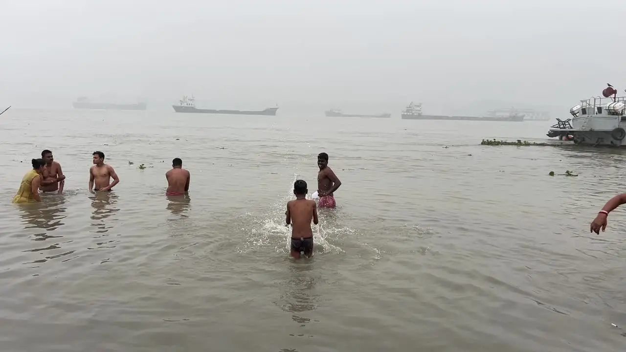 Profile view of people bathing and praying in foggy winter morning during Sankranti festival with jetty in the background