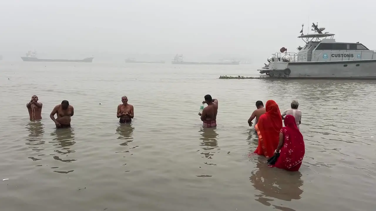 Static view of men and woman bathing and praying in a winter morning during Sankranti festival with jetty in the background in Babughat Kolkata