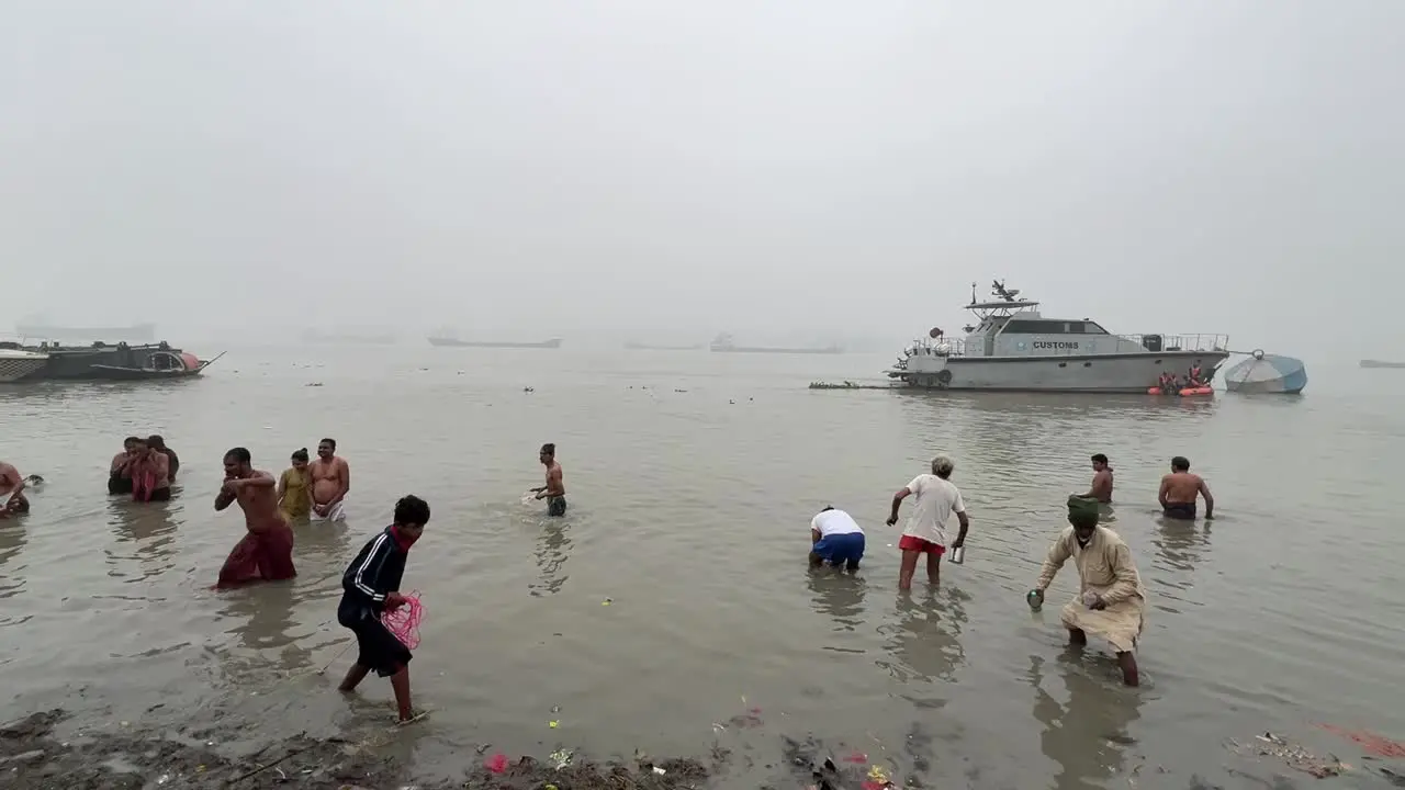 Men and woman bathing and praying in foggy winter morning during Sankranti with jetty in the background during a cold evening in Babughat Kolkata