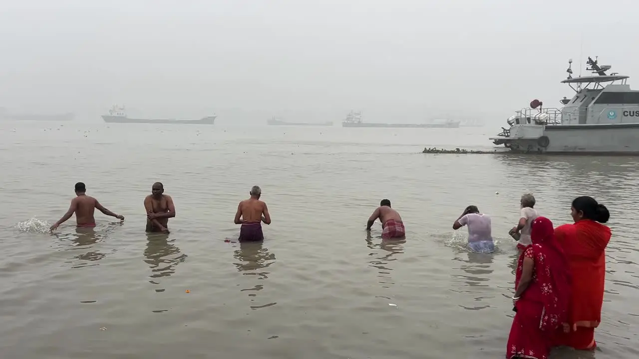 Rear view of few old men bathing at Babu Ghat in Kolkata with foggy seascape at background in India