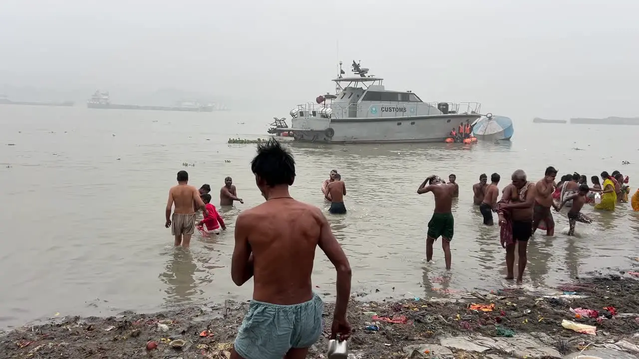 Wide shot of Hindus taking bath at Babu ghat for the celebration of Sankranti festival with ferries at background in Kolkata