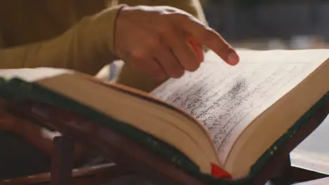 Close Up Of Open Copy Of The Quran On Stand At Home With Man Reciting Or Reading 1