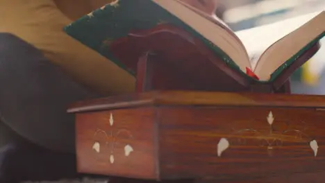 Close Up Of Open Copy Of The Quran On Stand At Home With Man Reciting Or Reading 2