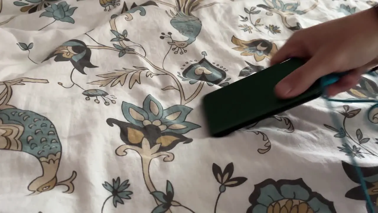 A power bank with a cable is placed on a bedspread with a flower and taken away again