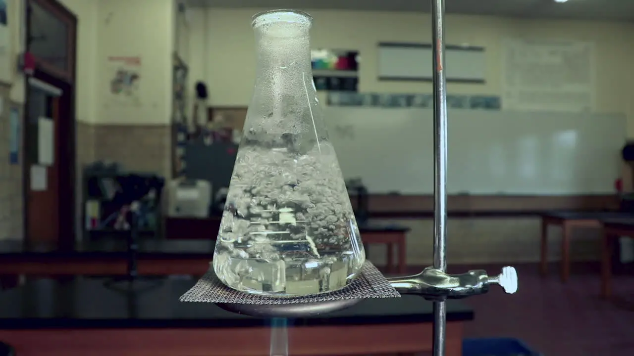 Water boiling in an erlenmeyer flask heated by bunsen burner in a chemistry classroom