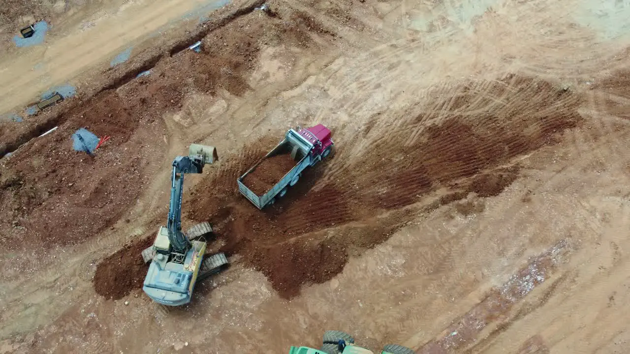 Excavator loads dump truck at construction site aerial perspective in 4K