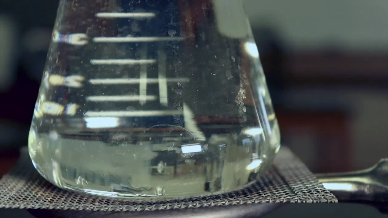 Close up of water beginning to boil in the bottom of an erlenmeyer flask