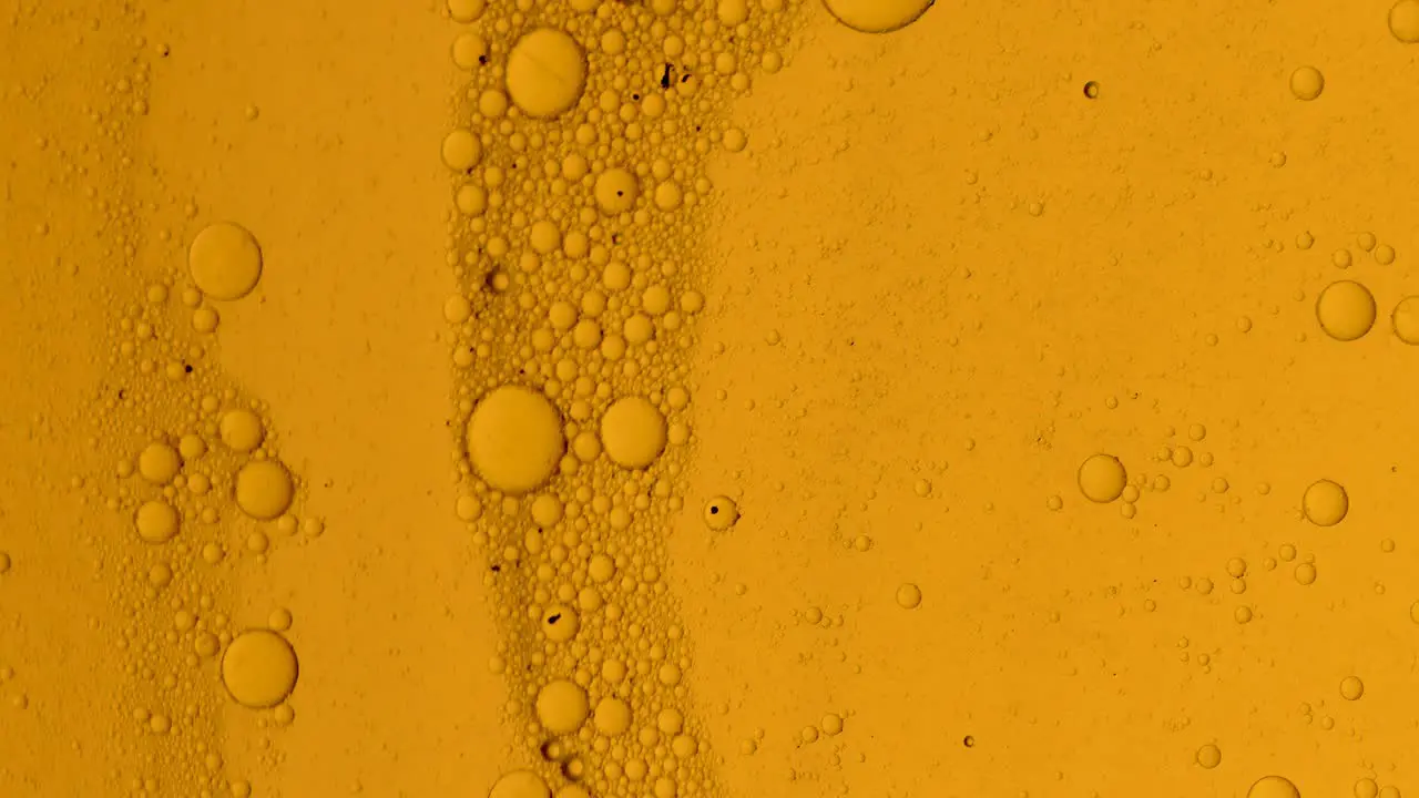 Dirty golden oil flow with black spots slowly with bubbles and dust on surface