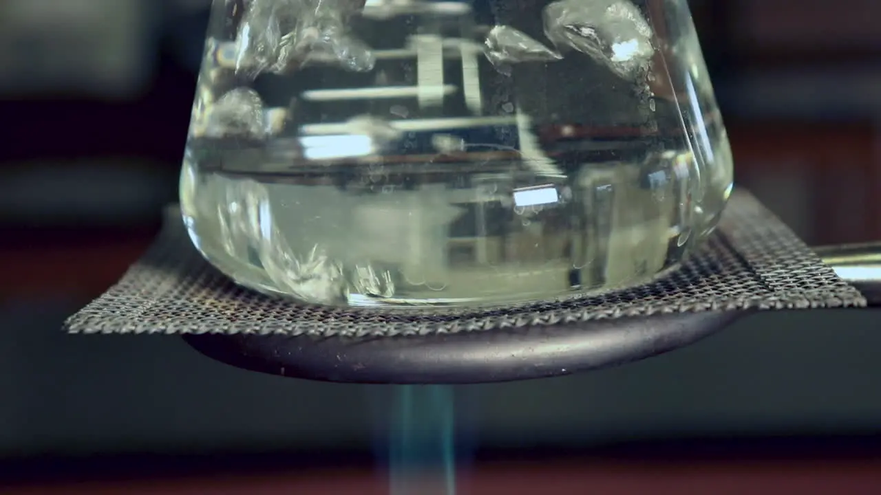 Close up of bottom of water boiling in an erlenmeyer flask on a ring stand heated by bunsen burner