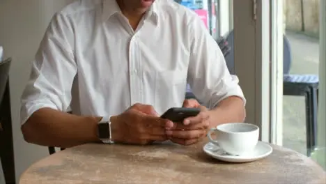 Male customer sitting in cafe using smartphone mid section