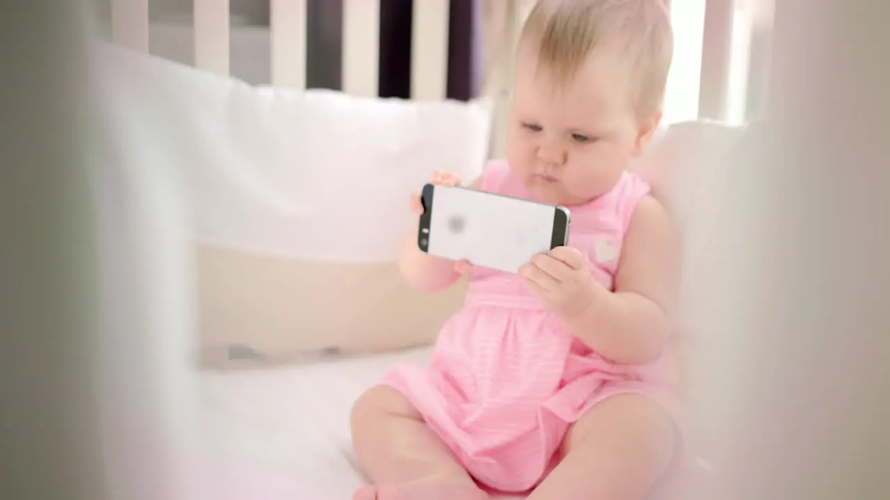 Little baby girl with phone in crib