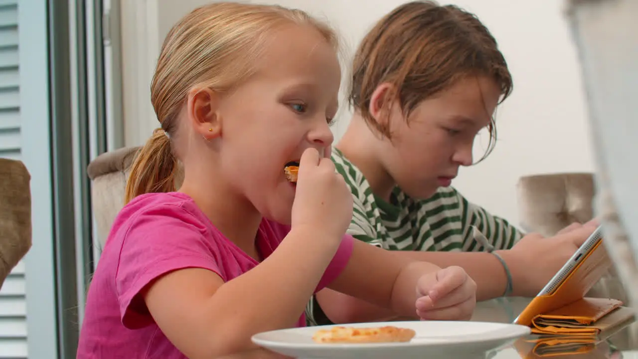 Siblings enjoying pizza and gadgets