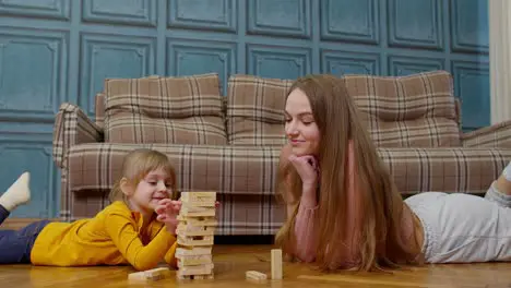 Happy young mother woman teaching small child daughter playing wooden blocks board game at home