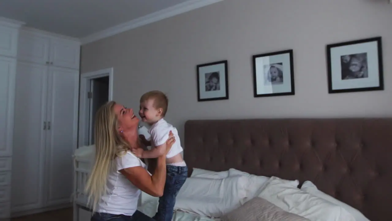 Mom and son are playing on the bed in a bright bedroom a boy of two years laughs and smiles