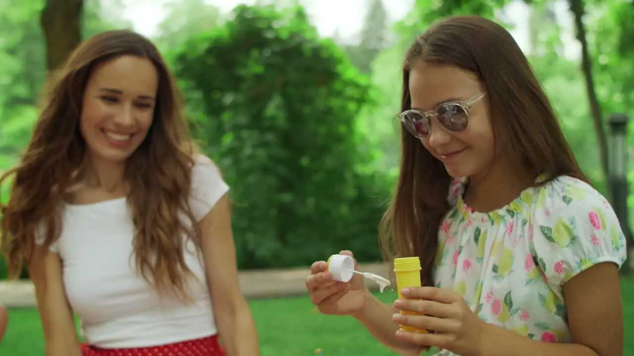 Woman and girl playing with soap bubbles in park Family laughing outdoors