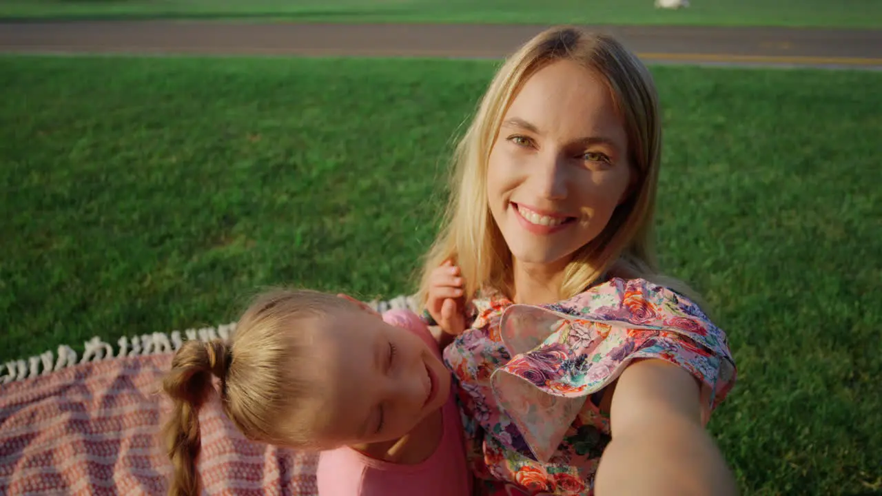 Happy woman hugging girl at meadow Young family taking selfie outdoor