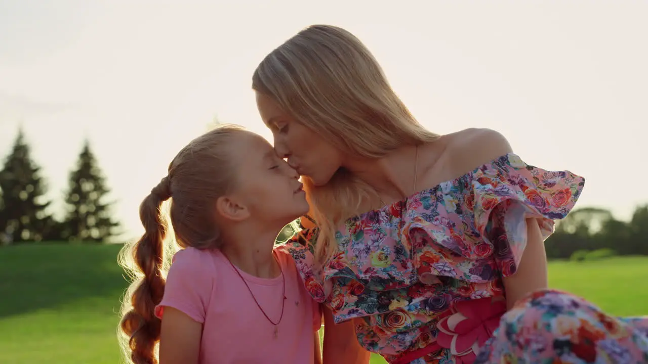 Happy woman kissing adorable girl in city park Family laughing outdoor