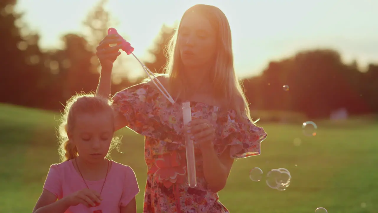 Happy family enjoying sunset in garden Woman with daughter blowing soap bubbles