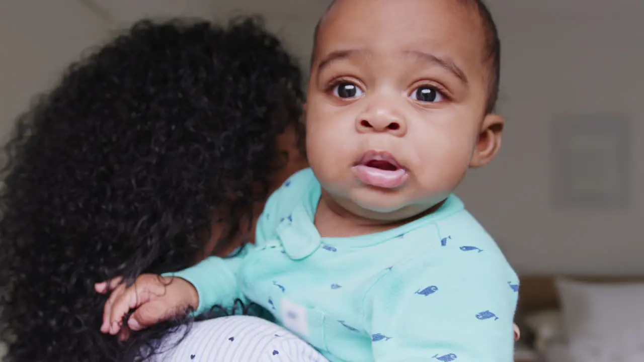 Loving African American Mother Wearing Pyjamas Cuddling Baby Son In Bedroom At Home