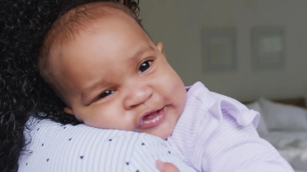 Loving African American Mother Wearing Pyjamas Cuddling Baby Daughter In Bedroom At Home