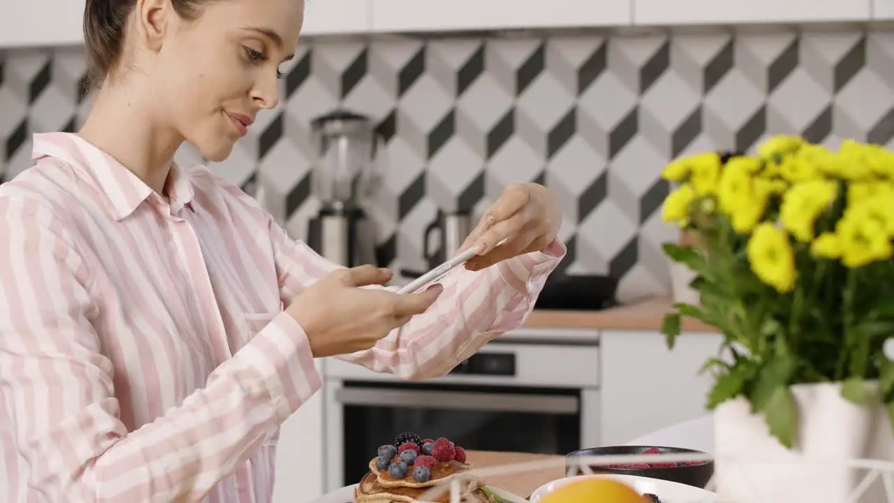 Woman photographing pancakes with fruit during breakfast in kitchen