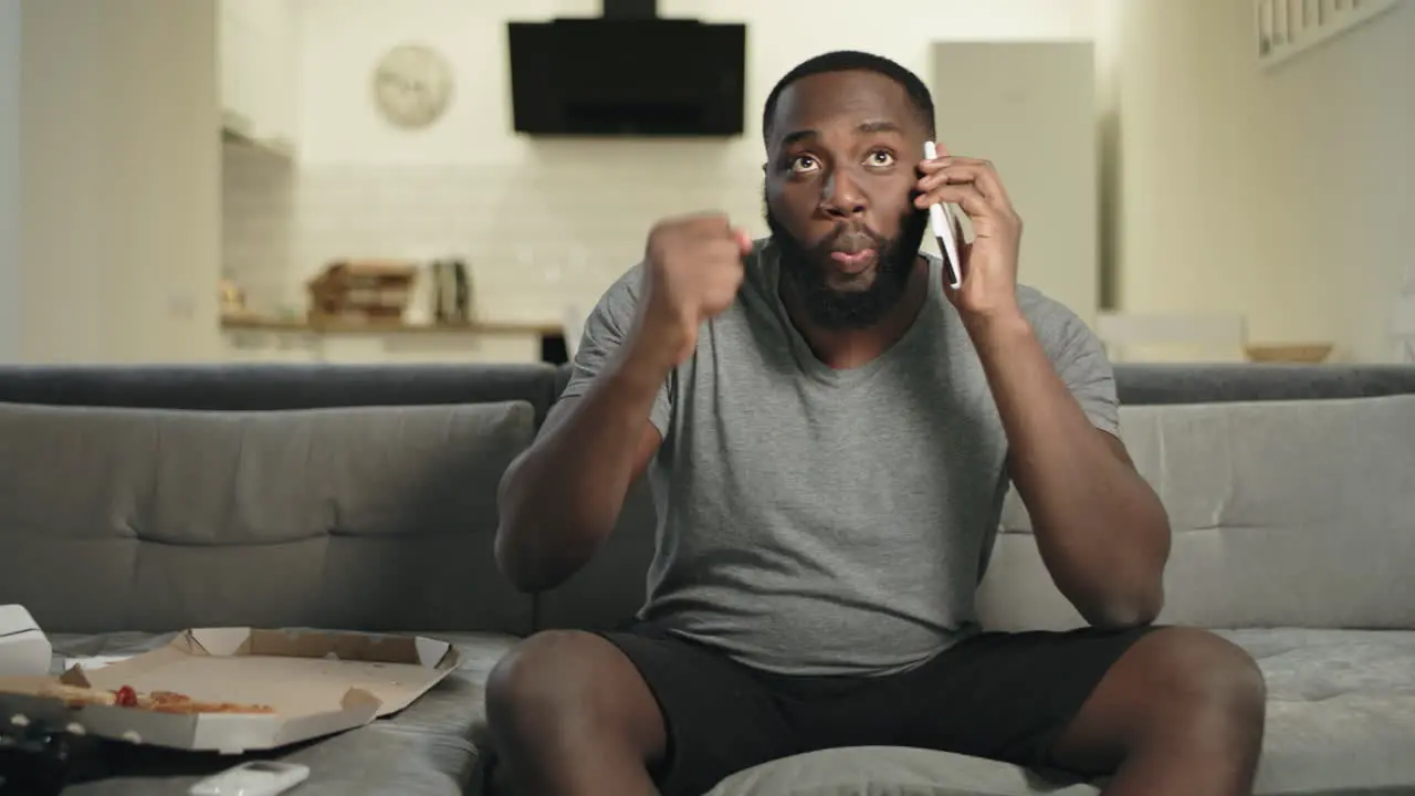 Black man eating pizza in front of tv Male fan commenting match results